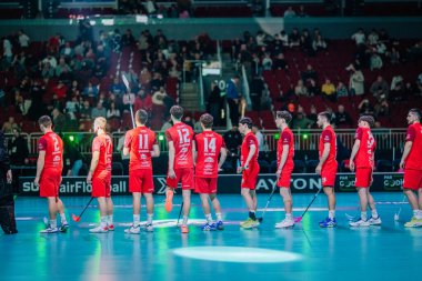 Riga, Letonya - 12 Nisan 2025 - Kırmızı üniformalı Floorball takımı, arka planda seyircinin olduğu kapalı spor salonundaki florball finalleri sırasında sırada bekliyor..