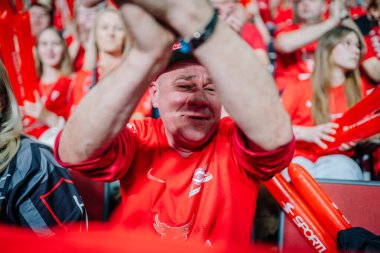 Riga, Letonya - 12 Nisan 2025 - Kırmızı tişörtlü fanatik, kırmızı tişörtlü, yüzünde kırmızı, heyecanlı ve tutkulu bir kalabalık, spor müsabakası boyunca tezahürat yapıyor..