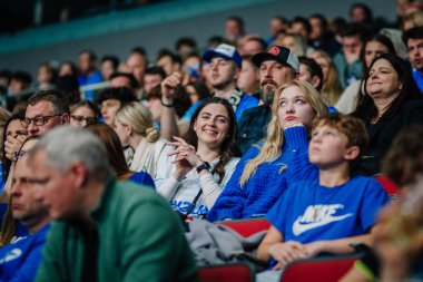 Riga, Letonya - 12 Nisan 2025 - Taraftarlar kapalı arenada zemin topu finallerini izliyorlar, kalabalıkta karışık duygular, mavi gömlekli insanlar heyecan, neşe, sıkıntı ve odaklanma gösteriyorlar.