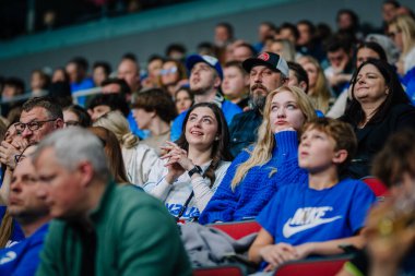 Riga, Letonya - 12 Nisan 2025 - Taraftarlar kapalı arenada zemin topu finallerini izliyorlar, kalabalıkta karışık duygular, mavi gömlekli insanlar heyecan, neşe, sıkıntı ve odaklanma gösteriyorlar.