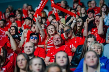 Riga, Letonya - 12 Nisan 2025 - Kırmızı tişörtlü fanatikler kapalı arenadaki zemin topu finallerinde kutlama yapıyor, el kaldırıyor, tezahürat yapıyor ve enerjik bir atmosfer yaratıyor..