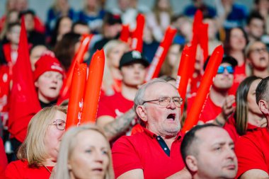 Riga, Letonya - 12 Nisan 2025 - Kırmızı tişörtlü ve aksesuarlı enerjik fanlar kapalı sahadaki finallerde yüksek sesle tezahürat yaparak heyecan ve takım ruhunu gösterdiler..