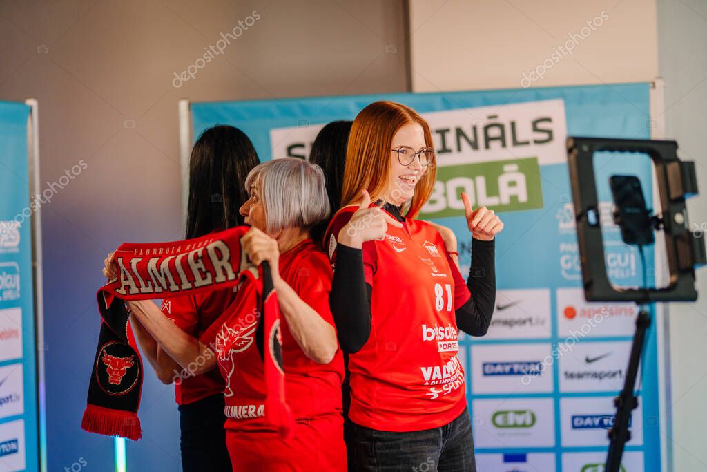 Riga, Latvia - April 12, 2025 - Group of female floorball fans in red jerseys enjoy a 360 video booth experience during the floorball finals event, smiling and dancing.