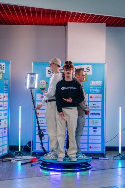 Riga, Letonya - 12 Nisan 2025 - Sponsor pankartları ve LED ışıkları ile çevrili 360 fotoğraf kabini platformunda poz verdi.