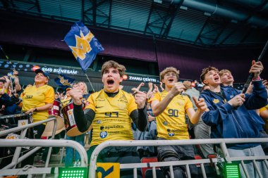 Riga, Letonya - 12 Nisan 2025 - Sarı tişörtlü hayranlar heyecan verici bir maç sırasında bayrak sallayarak ve takımlarını kutlayarak tribünlerde tezahürat yapıyorlar..