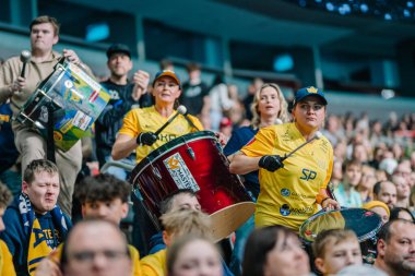 Riga, Letonya - 12 Nisan 2025 - Sarı ve mavi tişörtlü tutkulu fanlar tezahürat yapıyor, bayrak sallıyor ve trampet çalıyorlar..