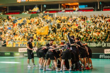 Riga, Letonya - 12 Nisan 2025 - Floorball takımı, taraftarların tezahüratlarıyla ve kalabalık arenada bayraklarını sallayarak final maçından önce bir çember oluşturuyorlar..