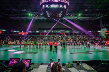 Riga, Letonya - 12 Nisan 2025 - Salon içi arenasında seyircilerin ve dramatik ışıklandırma efektlerinin yer aldığı iki florbol takımı ve hakem sahada sıraya dizildi.