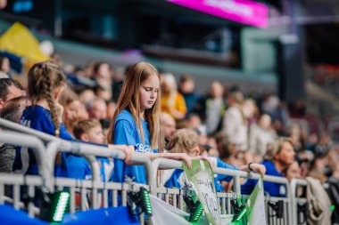 Riga, Letonya - 12 Nisan 2025 - Mavi formalı genç bir kız elinde el yapımı bir tabela, kalabalık bir arenada oynanan tenis finallerinde maçı ciddi şekilde izliyor..