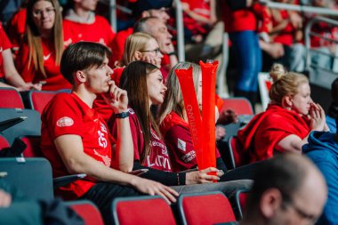 Riga, Letonya - 12 Nisan 2025 - Kırmızı tişörtlü genç taraftarlar tribünlerde oturup maçı dikkatle izlediler ve fan alkışları tuttular..