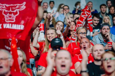 Riga, Letonya - 12 Nisan 2025 - Mutlu FBK Valmiera taraftarları kırmızı neşe içinde, gülümseyin ve tutkulu taraftarlarla dolu bir arenada, zemin topu finallerinde barış işaretleri gösterin.