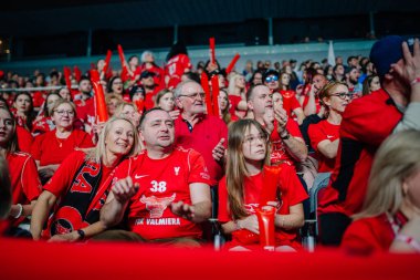 Riga, Letonya - 12 Nisan 2025 - Her yaştan kırmızı tişörtlü FBK Valmiera hayranları kalabalık kapalı bir arenada tutku ve takım ruhunu sergileyerek florbol finallerinin keyfini çıkarıyorlar..