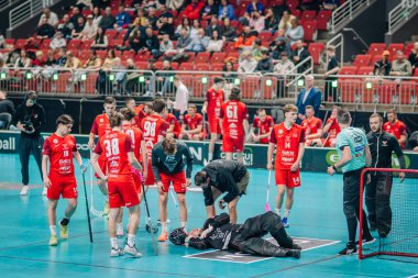 Riga, Letonya - 12 Nisan 2025 - Floorball oyuncuları, sağlık personeli ve bir hakem, yer topu finallerinde yaralı bir kalecinin etrafını sardı. Korttaki endişeli atmosfer.