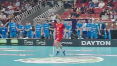 Riga, Letonya - 12 Nisan 2025 - Arka planda takım arkadaşları ve rakipleri olan kırmızı takım florbol oyuncusu yüksek bahisli finallerde hareket halindedir..