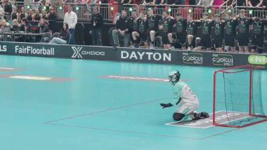 Riga, Letonya - 12 Nisan 2025 - Beyaz formalı florbol finalleri oyuncusu, kaleci gergin atmosferde kaleyi savunmak için beklerken penaltı atışı yapıyor..