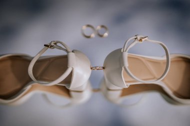 Beyaz gelinlik ayakkabıları ve altın nişan yüzükleriyle zarif bir düğün kompozisyonu yansıtıcı bir yüzeye yumuşak ışıkla yerleştirilmiş..