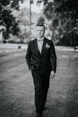 Valmiera, Letonya - 9 Ağustos 2024 - Takım elbiseli ve papyonlu damat, düğün gününde şık siyah-beyaz bir portrede, güvenli bir şekilde dışarı çıkar..