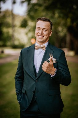 Valmiera, Letonya - 9 Ağustos 2024 - Donanma takımlı ve altın papyonlu gülen damat, düğün gününde güven ve neşe saçar..