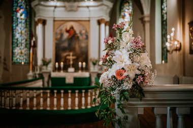 Valmiera, Letonya - 9 Ağustos 2024 - Arka planda sunak bulunan dekore edilmiş bir kilisede zambaklar, bebek nefesi ve pembe çiçeklerle bir düğün çiçeği aranjmanının yakın çekimi