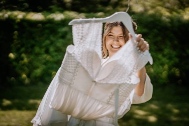 Neşeli bir gelin gelinliğini kaldırıyor, güneşli bir bahçede ışıl ışıl gülümsüyor, özel günü için heyecanla dolu..