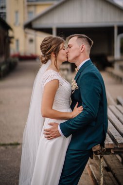 Gelin ve damat, düğün günlerinde dışarıda romantik bir öpücük paylaşıyorlar. Kırsal bir ortamda birbirlerine sevgi ve neşeyle sarılıyorlar..