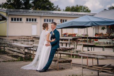 Valmiera, Letonya - 9 Ağustos 2024 - Yeni evli bir çift, damat bankta oturuyor ve gelin birbirine gülümsüyor..