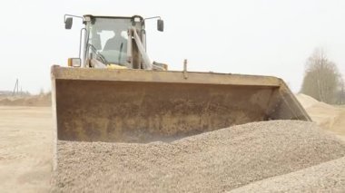 Valmiera, Letonya - 16 Nisan 2025 - Bir ön yükleyici kovasını çakılla doldurur ve sonra çakılları sanayi bölgesindeki bir yığının üzerine döker.