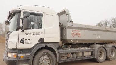Valmiera, Letonya - 16 Nisan 2025 - Yüklü beyaz bir İskandinav kamyonu malzeme teslimatını tamamladıktan sonra kumlu bir sanayi bölgesinden yavaşça uzaklaşır..