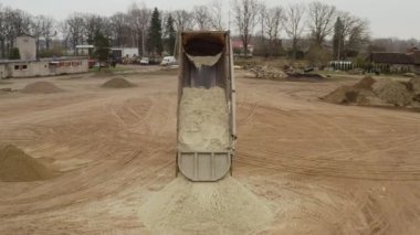 Valmiera, Letonya - 16 Nisan 2025 - Arkadan kum boşaltan bir damperli kamyonun havadan görünüşü, toprak yığınlarıyla çevrili geniş bir inşaat sahasında bir tepe oluşturur..