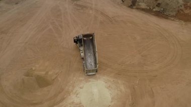 Valmiera, Letonya - 16 Nisan 2025 - Yüklü bir çöp kamyonu, toprak yığınlarıyla çevrili bir inşaat sahasına soluk kum yükünü boşaltıyor. Havadan görüş, düzgün iniş görüntüsü.