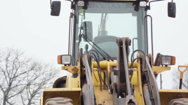 Valmiera, Letonya - 16 Nisan 2025 - Bulutlu bir günde hidrolik kollar, ışıklar ve taksi detaylarını gösteren sarı bir Volvo yükleyicinin yakın görüntüsü.