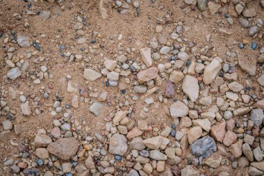 Kum ve küçük ve orta büyüklükteki doğal taşlar ve çakıl taşlarının karışımı yere saçılmış sert, toprak dokulu bir yüzey oluşturur..