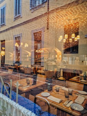 Milan, İtalya - 10 Mart 2025 - Kırsal tuğla kemerler, zarif avizeler ve sıcacık bir ortam ile düzenli yemek masaları gösteren bir restoran penceresinden bakın.