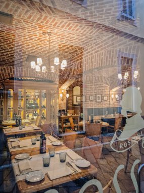 Milan, İtalya - 10 Mart 2025 - Pencereden görünen şık bir restoran içi, set ahşap masalar, açık tuğla kemerler, sıcak ışıklandırma ve rahat bir ortam..