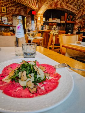 Milan, İtalya - 5 Nisan 2025 Biftek carpaccio, roka, trüf, parmesan ve köpüklü su ile nefis bir restoran masası..