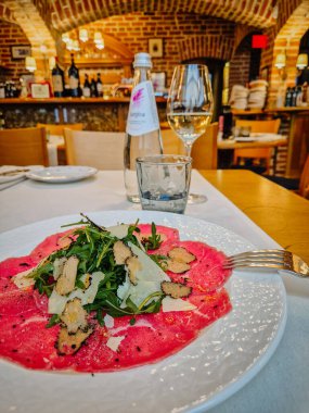 Milan, İtalya - 5 Nisan 2025 Biftek carpaccio, roka, trüf, parmesan ve köpüklü su ile nefis bir restoran masası..