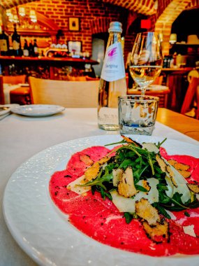 Milan, İtalya - 5 Nisan 2025 Biftek carpaccio, roka, trüf, parmesan ve köpüklü su ile nefis bir restoran masası..