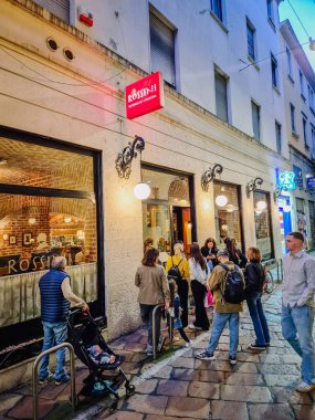 Milano, İtalya - 5 Nisan 2025 - İnsanlar akşamları bir kaldırım taşı sokağında sıcak bir restoranın önünde toplanarak canlı ve davetkar bir şehir atmosferi yarattılar..