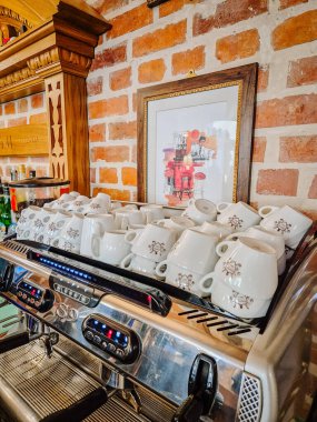 Milan, İtalya - 5 Nisan 2025 - Espresso makinesi seramik bardakları yığılmış bir kafeteryada veya restoranda, üzerinde çerçeve çerçeveli sanat eserleri olan tuğla bir duvara karşı