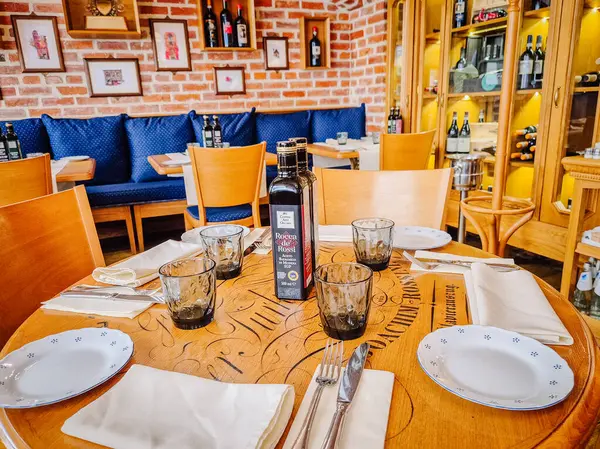 Milan, İtalya - 5 Nisan 2025 - Ahşap mobilyalar, şarap şişeleri ve rahat dekorlu bir restoranda yemek masası kurun. Zeytin yağı şişesi süsü. Sıcak, davetkar atmosfer.