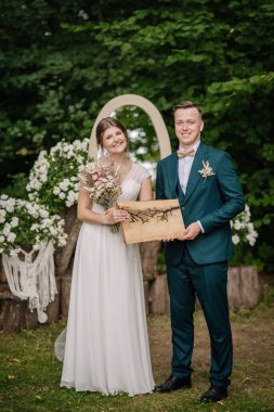 Gelin ve damat, Lichtenberg sanatı ile tahta bir tahta tutarak dışarıda gülümsüyor. Etrafı çiçeklerle, buketlerle ve yeşilliklerle çevrili..