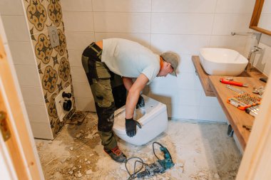 Bir inşaat işçisi, tadilat altındaki bir banyoya, tamamlanmamış döşeme döşemelerine ekipman ve döküntüler döşeyen bir tuvalet kuruyor..