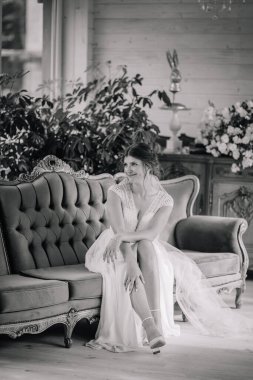 Dantelli gelinlik içindeki gelin klasik bir iç mekânda klasik bir kanepede zarif bir şekilde oturur..