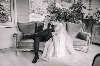 Gelin ve damat antika bir kanepede oturur, sessiz ve sevgi dolu bir anı paylaşırlar. Siyah ve beyaz tonu düğün resmine sonsuz zarafet katıyor..