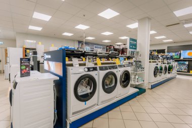 Valmiera, Letonya - 23 Nisan 2025 - Parlak ışıklandırma altında sergilenen geniş çaplı çamaşır makineleri, kurutma makineleri ve küçük mutfak gereçleri içeren elektronik mağaza koridoru.