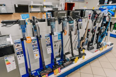Valmiera, Letonya - 23 Nisan 2025 Philips, Samsung ve Tefal gibi markaların kablosuz elektrik süpürgelerinin beyaz ve mavi stantlarda düzgün bir şekilde dizilmiş halleri..