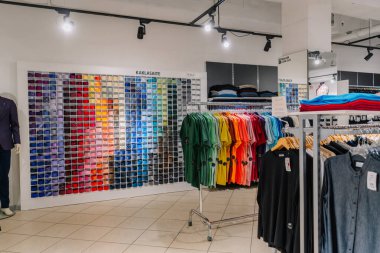 Valmiera, Letonya - 23 Nisan 2025 - Parlak ışık altında renklere göre dizilmiş tişört askıları ve gölgeli kravatlardan oluşan renkli bir duvar ile Mens moda mağazası