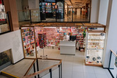 Valmiera, Letonya - 23 Nisan 2025 - Bir alışveriş merkezindeki renkli aksesuar, duvardan duvara saç bağları, mücevherler ve biblolar, yukarıdan bir merdiven ve cam parmaklıkların yanından görülüyor..