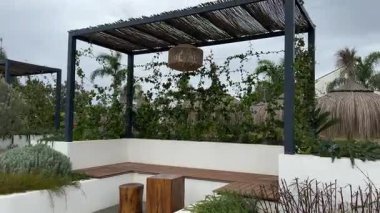 Tırmanış asmaları, ahşap koltukları ve tropikal bir bahçede sazdan şemsiyeler ve palmiye ağaçlarıyla örülü bir pergola..