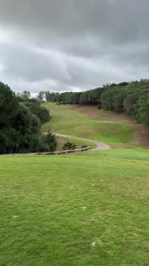 İspanya 'nın Sotogrande şehrinde bulutlu bir günde yoğun çam ağaçlarının arasından süzülen tepelik golf pistinin geniş manzarası..